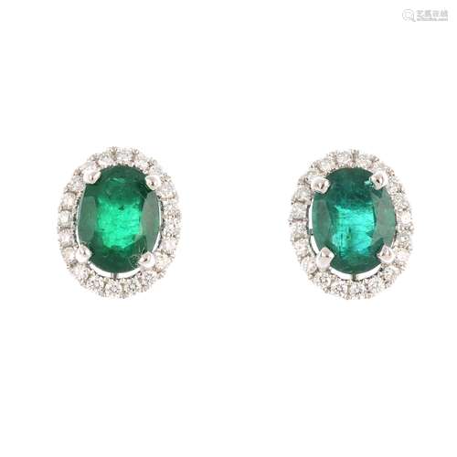 A pair of emerald and diamond cluster earrings. Each designed as an oval-shape emerald, with