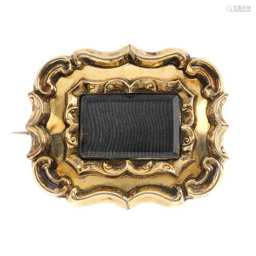 A late Victorian memorial brooch. The rectangular-shape glazed panel, with scrolling surrounds.