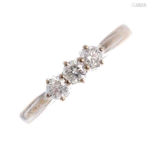 An 18ct gold diamond three-stone ring. The brilliant-cut diamond line, with grooved shoulders and