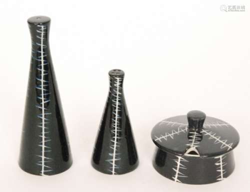 A 1950s Clayburn Pottery three piece cruet set designed by Jessie Tait comprising tall salt pot, squat pepper and a mustard pot and cover, each decorated in a black glaze with white carved linear banding, unmarked. (3)