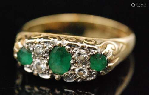 A 1970s 18ct emerald and diamond boat head ring, central oval cut emerald with two round cut emeralds, spaced by two pairs of old round cut diamonds, scroll head setting to tapering band, ring size O