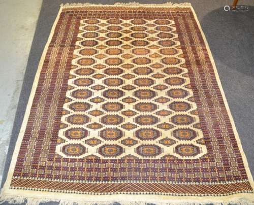 A 20th Century Persian Bokhara rug, with four rows of thirteen elephants foot pattern maroon and amber coloured medallions upon the central oatmeal coloured field, interspersed with smaller medallions, all within repeat pattern borders, 258cm x 185cm.