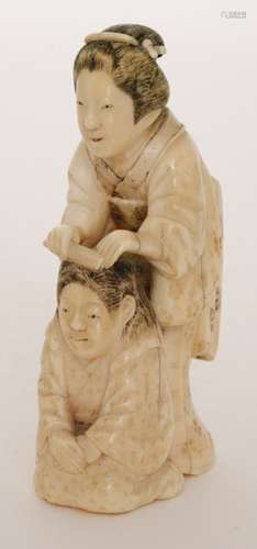 A Japanese Meiji period carved ivory okimono of a Geisha combing the hair of a maiko dancing girl kneeling before her, both with black stained and engraved hair and kimono, red stained lips and hair decorations, height 11cm.