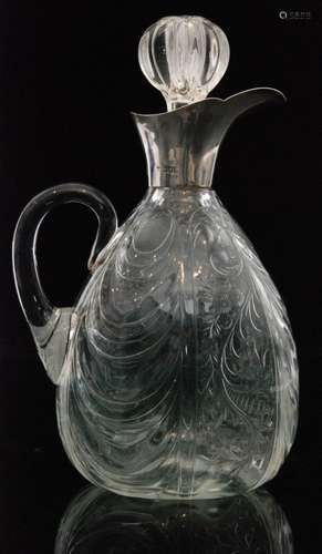 An early 20th Century Stevens & Williams clear crystal glass claret jug of ovoid form in the rock crystal style, intaglio cut and polished with repeat panels of floral scrolling and swag motives all below a London hallmarked silver collar and associated stopper, unmarked, height 23cm.