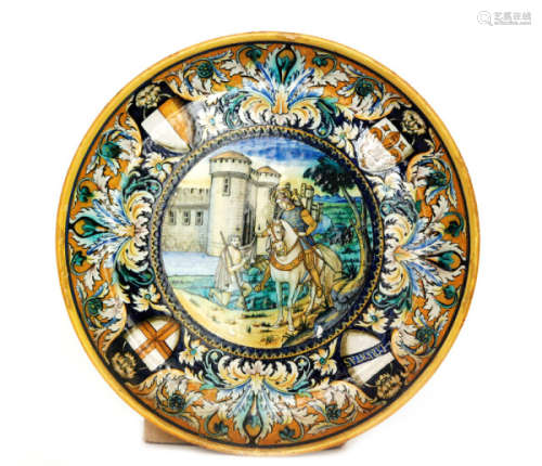 An early 20th Century Cantagalli maiolica charger decorated in the Renaissance style with a central roundel depicting St. Martin of Tours and a kneeling man with a castle and moat in the background, the border edge with four shields each hanging from the mouth of a lion within acanthus leaves and to a blue ground, painted cockerel mark, diameter 47cm