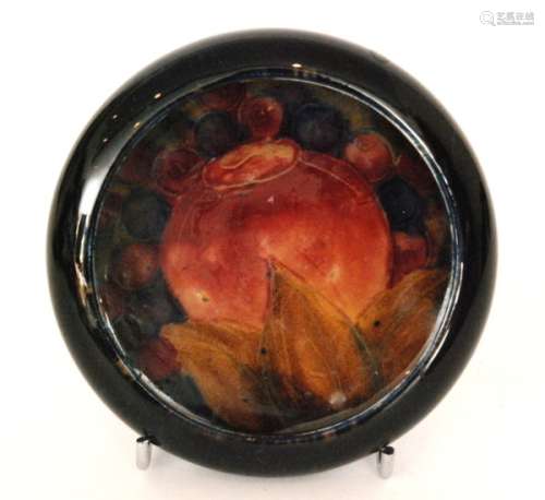A Moorcroft roll rim pin dish decorated in the Pomegranate pattern, the central well with a large single fruit surrounded by berries against a blue wash ground, impressed mark and initialled in green, diameter 11cm