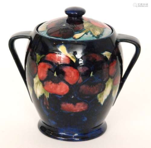 A Moorcroft twin handled biscuit barrel of tapering form decorated in the Pansy pattern with a band of flowers and foliage against a dark blue ground, the slightly domed cover with three tubelined flowers against a lighter blue ground, impressed mark and initialled in blue, height 18cm, restored