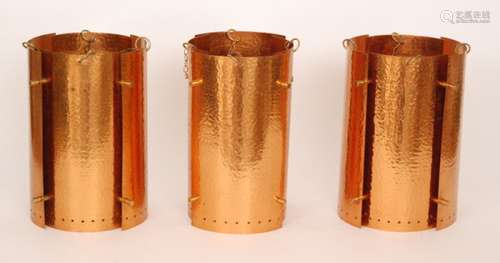 A set of three mid 20th Century modernist beaten copper light fittings each of cylindrical form, height 30cm (excluding the hanging chains)