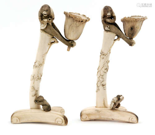 A pair of late 19th Century Japanese bone candlesticks in the form of monkeys perched on a fruiting bough and holding a flower head between their feet, above a shaped tricorn base with an infant below, height 24cm (2)