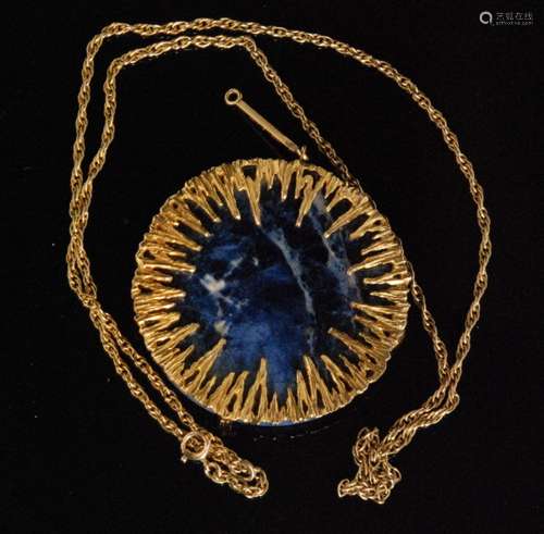 A 1970s hallmarked 9ct mounted circular lapis lazuli pendant of modernist design, the textured gold frond frame with claw set lapis lazuli suspended from an elongated gold bar bale and Prince of Wales link chain, diameter 5cm, Birmingham 1973.