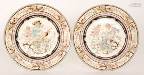A pair of early 20th Century Rudolf Ditmar Hungarian majolica chargers, each relief moulded and in tones of pink, grey, cream and blue, the first with a lady reading a love letter with cupid by her side, the second with a seated gentleman holding a lute received a letter from cupid, both with impressed Znaim marks, diameter 35cm