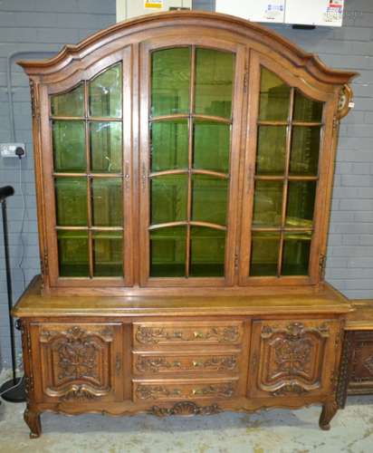 A 20th Century oak cabinet bookcase in the French taste, the arched upper section with three glazed doors enclosing adjustable shelves, all over the base section fitted with three drawers flanked by a cupboard at either side, with a shell carved apron and scroll front feet, height 205cm and width 167cm, S/D.