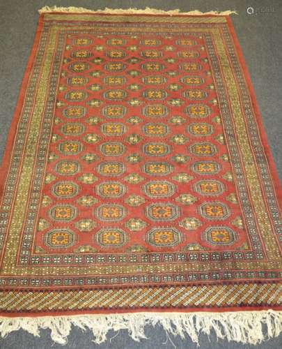 A 20th Century Persian Bokhara rug, with four rows of twelve elephants foot pattern amber, oatmeal and blue coloured medallions upon the central rust coloured field, interspersed with smaller medallions, all within repeat pattern borders, 272cm x 183cm.