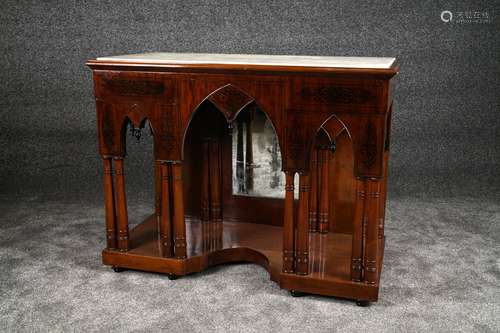 Console “à la cathédrale“. Sommée d'un marbre blanc. Large ceinture présentant une arcature en ogive supportée par une double colonne. Fond miroir. Base découpée et petits pieds tournés. Acajou marqueté de palmettes en ébène. Travail du second quart du XIXe siècle. Dimensions: 98 x 129 x 60 cm.