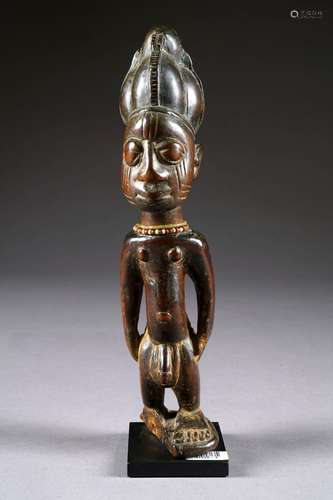 Ibeji - Yoruba. Figurant un homme debout, les mains posées sur les cuisses. Visage scarifié, coiffe formée d'un long chignon en pointe, cou paré d'un double collier de perles. Bois sculpté à patine sombre et luisante. Nigeria. Hauteur: 30 cm. Sur socle. (Accident). Provenance: ancienne collection de Madame J. de L. à Bruxelles. Acquis dans les années 70 à Monsieur Emile Deletaille. Vendu pour cause de succession au profit de diverses associations.