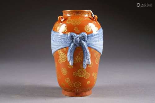 Vase en Forme de jarre. Au col présentant quatre passants et à panse ceinturée par un ruban noué en trompe l'oeil. Décor, sur fond corail, d'un semis de fleurs or sur fond corail. Porcelaine de Chine. Marque sigillaire de Kien-Long. Hauteur: 20,5 cm. Condition: Pas d'accident ni de restauration. Saut d'émail sur le fond.