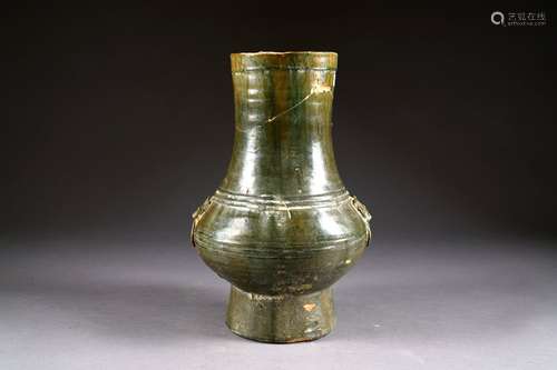 Vase Han de Forme Hu. A long col tubulaire et à panse moulurée. Prises simulant des anneaux retenues chacune par un taotie. Céramique à glaçure vert de cuivre à l'imitation du bronze. Hauteur: 38,5 cm. Condition: Col accidenté, éclats, restauration.