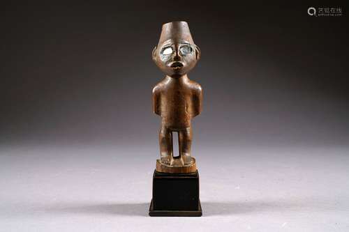 Fétiche Vili. Figurant un personnage debout aux membres schématisés. Yeux formés de deux éclats de verre. Bois sculpté et patiné. République démocratique du Congo. Hauteur: 20 cm. Sur socle.