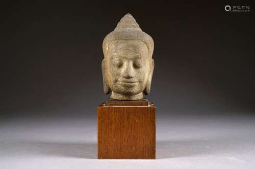 Tête de Bouddha. Au visage apaisé et légèrement souriant. Longues oreilles descendant au niveau du cou. Coiffe bouclée sommée d'un chignon. Grès sculpté. Art Khmer de style Bayon. XIIe/XIIIe siècle. Hauteur: 20 cm. Sur socle en noyer. Hauteur totale: 33 cm. Provenance: collection particulière. Pas de certificat.