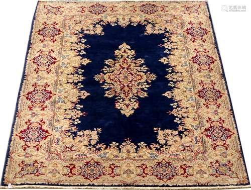 Carpette Kirman. Le fond, bleu nuit, présente un pourtour de petites fleurettes. Bordure à cartouches rouges. Dimensions: 250 x 150 cm.