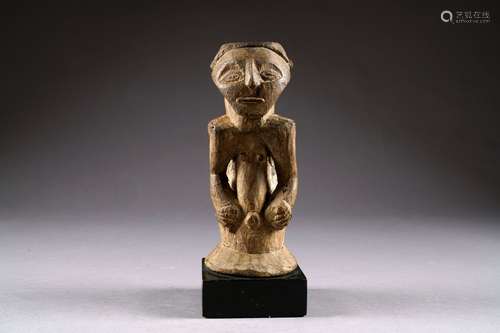 Kusu. Fétiche en buste au visage triangulé et aux yeux en amande. Tronc effilé encadré par les bras aux mains posées sur l'abdomen. Bois sculpté. République démocratique du Congo. Hauteur: 28 cm. Sur socle.