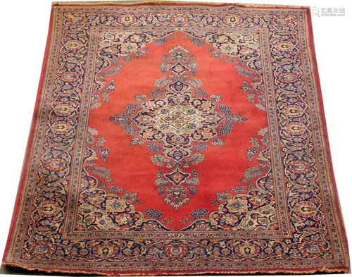 Carpette Kashan. Le fond, rouge uni, présente un long médaillon central. Ecoinçons chantournés et bordure florale à fond bleu nuit. Dimensions: 211 x 134 cm.