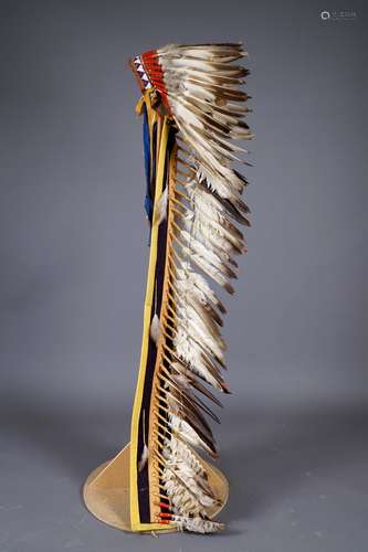 Grande Coiffe Sioux à longue Traîne. Bonnet en cuir, orné d'une frise de perles sur la partie frontale, retenant une traîne de feutrine brune et jaune. L'ensemble retenant des plumes d'aigle ligaturées à de petits rouleaux de feutrines. Etats-Unis. XXe siècle. Hauteur: 190 cm. Provenance: collection particulière.