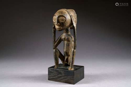 Hemba. Ancienne statue d'ancêtre figurant un homme assis, les mains posées sur les tempes. Visage aux yeux en amande et souligné d'un fin collier de barbe. Coiffe à motifs géométriques. Bois sculpté et patiné. République démocratique du Congo. Hauteur: 24 cm. Sur socle. Provenance: collection particulière belge.