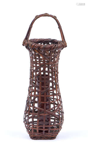 A tall and round dark brown wickerwork ikebana basket with a fixed handle