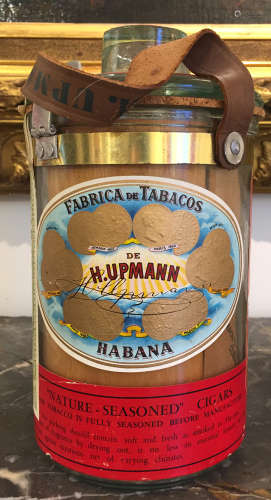 H.UPMANN, HABANA, vers 1960-1970 Amusant pot à cigares en verre, fermetures en métal, multiples étiquettes de garantie collées, bien complet de ses feuilles de cèdre portant les armes de Upmann.  Haut.: 19 cm Bon état