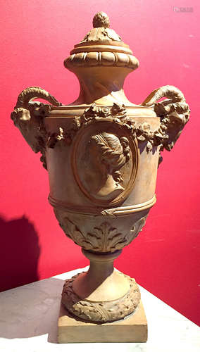 VASE MEDICIS en terre cuite sur piedouche à prises latérales à têtes de bouc retenues par des guirlandes tombantes, le corps orné d'un médaillon central toutes faces à profil de jeune fille, Socle carré à couronne de laurier. Le frétèle à pomme de pin. Fin XIXème siècle Haut : 52 cm (quelques accidents)