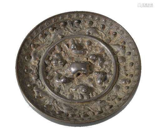 A Chinese bronze mirror, Tang Dynasty, cast with a central knop formed by a crouching beast