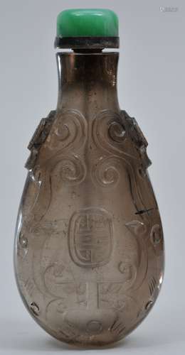 Snuff  bottle. China. 19th century. Elongated gourd shape. Smoky quartz with the surface carved with scrolling dragons and shou characters. Well hollowed. Apple green Jadeite stopper. 3-1/8