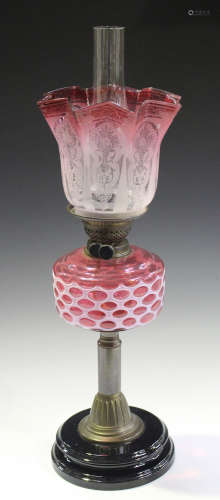 A late Victorian brass table oil lamp with an acid etched shade and a cranberry overlaid reservoir