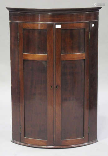 An early 19th century mahogany bowfront hanging corner cabinet