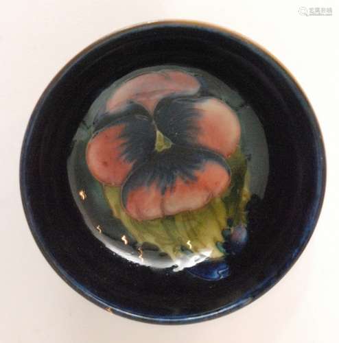 A small Moorcroft Pansy pattern footed bowl decorated with a central pink flower against a blue ground