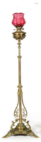 A Victorian brass standard lamp with pierced column on scroll cast base with ruby moulded shade