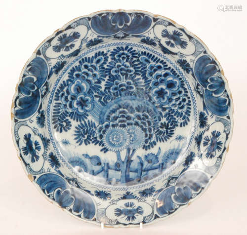 A late 19th Century Delft tin glaze plate decorated in blue and white with a large spray of flowers within a patterned border edge