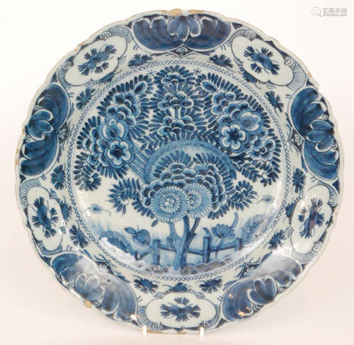 A late 19th Century Delft tin glaze plate decorated in blue and white with a large spray of flowers within a patterned border edge