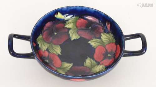 A William Moorcroft twin handled pedestal bowl decorated in the Pansy pattern with tubelined flowers and foliage against a blue ground