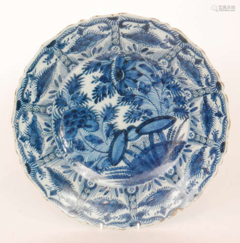 A late 19th Century Delft tin glaze plate decorated in blue and white with a large spray of flowers within a patterned border edge