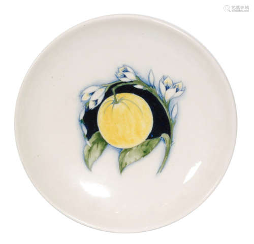 A 1930s William Moorcroft charger decorated in the Orange and Blossom pattern with a central tubelined fruit against a dark ground and framed with snowdrops