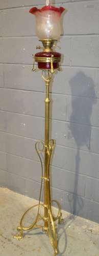 An Edwardian Art Nouveau style brass standard lamp on swept open work base and floral feet with ruby reservoir and etched shade