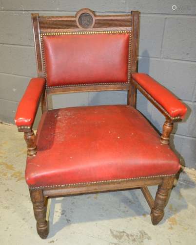 A Victorian oak elbow chair with central armorial back upholstered in red leather