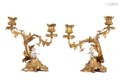 A PAIR OF LATE 19TH CENTURY ROCOCO STYLE GILT BRONZE AND PORCELAIN FIGURAL CANDELABRAthe asymmetric candlesticks modelled as scrolling acanthus leaves and flowers