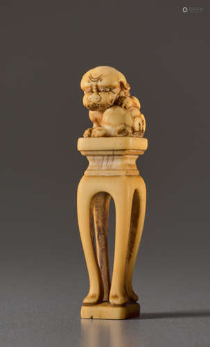 AN IVORY NETSUKE OF A SHISHI ON A PEDESTALIvory...