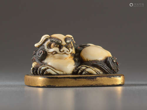 AN IVORY AND LACQUER NETSUKE OF A RECUMBENT SHISHI...