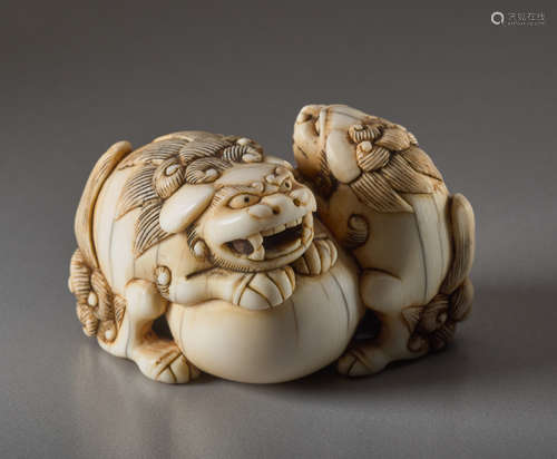 AN IVORY NETSUKE OF TWO SHISHI AND BALLIvory ne...