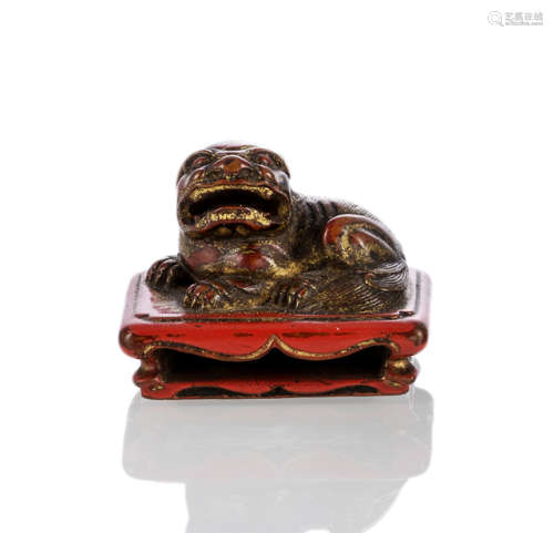 A CARVED AND LACQUERED AND PART-GILT WOOD NETSUKE OF A LION ON A LOW-TABLE