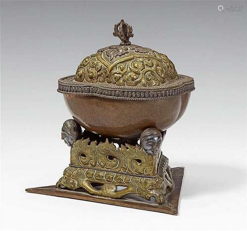 A Tibetan copper kapala with a brass lid and stand with silver details